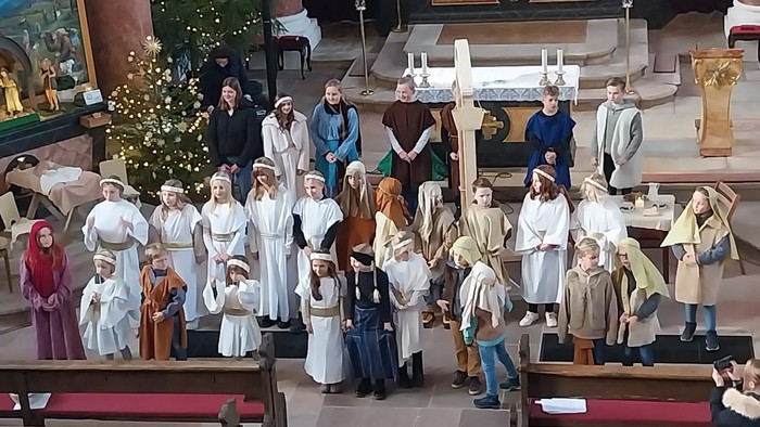 Gruppe von Kindern und Erwachsenen in historischen Kostümen, die in einer geschmückten Kirche während einer festlichen Veranstaltung auftreten.