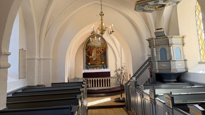 Elegant kirkeinteriør med hvælvede lofter, kirkebænke og prægtige lysekroner, der oplyser alterområdet.