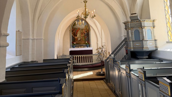 Elegant kirkeinteriør med hvælvede lofter, kirkebænke og prægtige lysekroner, der oplyser alterområdet.