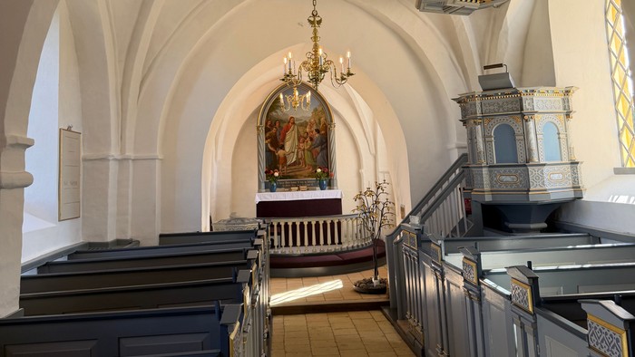 Elegant kirkeinteriør med hvælvede lofter, kirkebænke og prægtige lysekroner, der oplyser alterområdet.