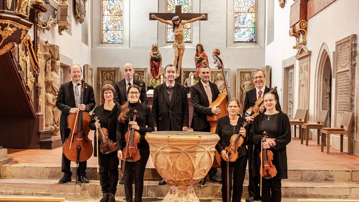 Musizierende des Ambrosius-Kammerorchester Eisenach stehen an Bachs Taufstein