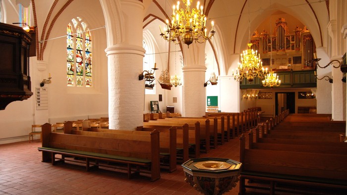 Innenraum einer Kirche mit hölzernen Bänken, Kronleuchtern und einem Altar.