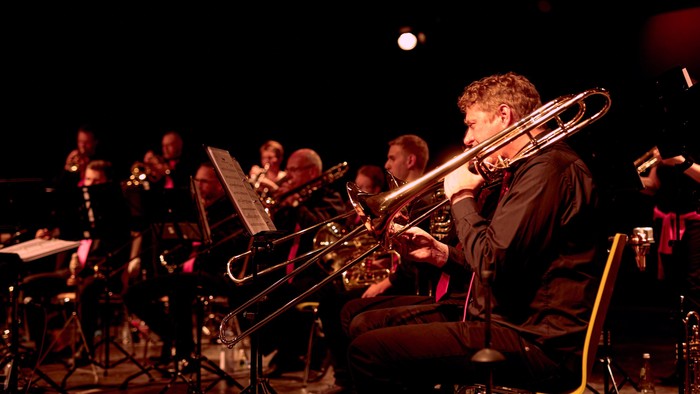 Ein Posaunist tritt mit einem konzentrierten Blechbläserensemble während eines Konzerts auf der Bühne auf.