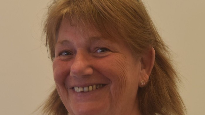 Smilende kvinde med briller iført en hvid bluse og perlekæde.