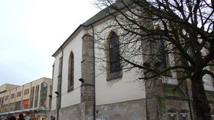 Kirchengebäude mit hohen schmalen Fenstern in der Fußgängerzone.