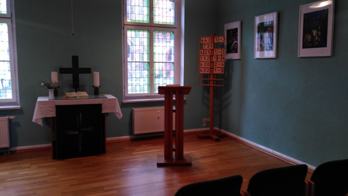 Ein Kirchenraum mit Altar, Stühlen und Bildern an der Wand