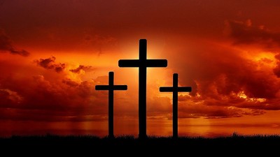 Drei Kreuze vor einem blutroten bewölktem Himmel.