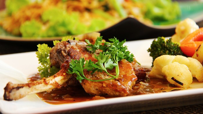 Grillstegt kyllingelår med grøntsager, garneret med friske urter og en lækker sovs på en hvid tallerken.