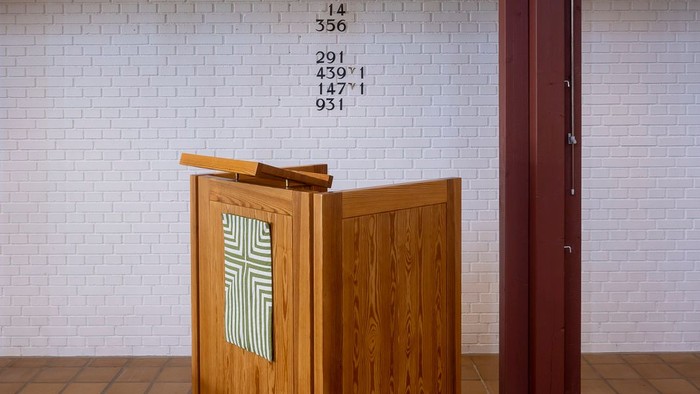 En træpult i kirke med korset på forside og en liste med tal på bagside