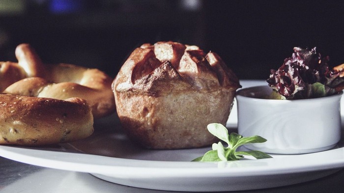 Ein rustikaler Teller mit einem gebackenen Muffin, Gebäck und einer Beilage Salat, garniert mit frischen Kräutern.