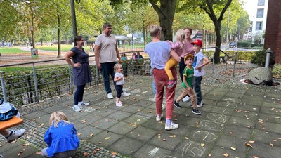 En gruppe børn og voksne spiller på en plæne med tegnede hoppebænke.