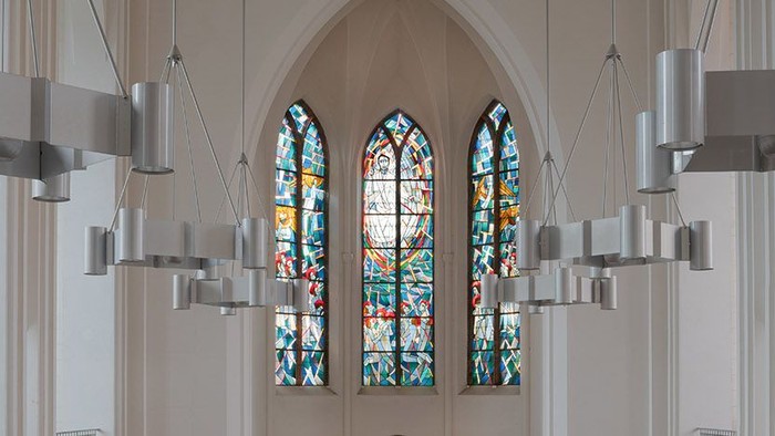 Ein Kircheninneres mit farbenfrohen Buntglasfenstern und modernen Lichtern.