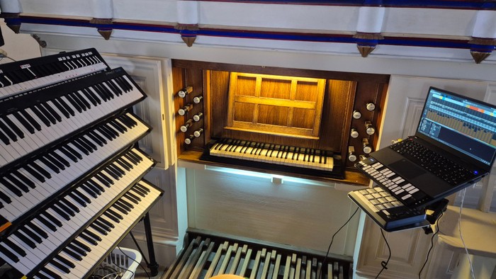 Eine detaillierte Ansicht einer Orgelkonsole mit mehreren Manualen, Bedienfeldern und digitaler Audiotechnik.