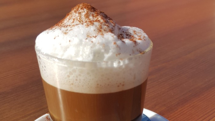 Ein Glas Kaffee mit Sahne und Zimt auf einem Teller mit Löffel