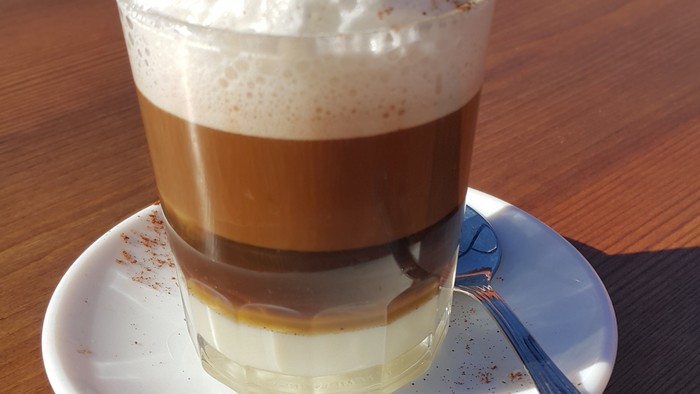 Ein Glas Kaffee mit Sahne und Zimt auf einem Teller mit Löffel