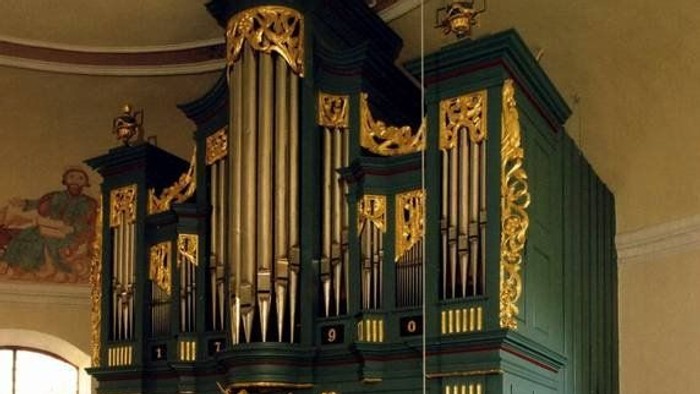 Komplexe historische Pfeifenorgel mit aufwendigen Goldverzierungen und grünen Paneelen in einer Kirche.