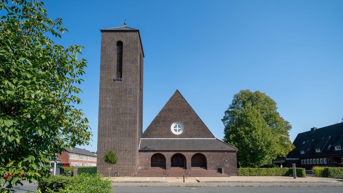 Backsteinkirche mit hohem Turm und dreieckigem Dach, umgeben von Grünflächen.