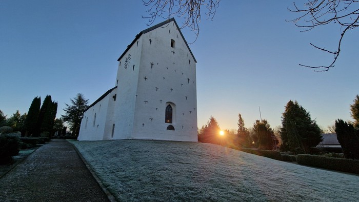 Nørre Snede kirke fra tårnsiden med rimfrost på græsset og et glimt af den nedgående sol