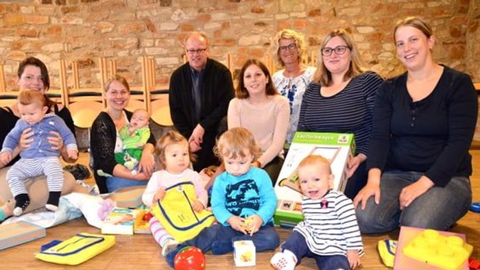 Gruppe von Erwachsenen und Kindern, die glücklich zusammen drinnen posieren, mit verschiedenen bunten Spielzeugen und Kisten.