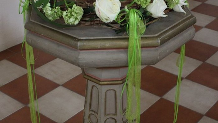 Ein kleiner Tisch mit weißer Kerze und grünen Blumen.