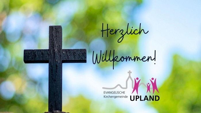 Ein einladendes Kreuz mit der Aufschrift „Herzlich Willkommen“ und dem Logo der Evangelischen Kirchengemeinde Upland in einer grünen Außenumgebung.