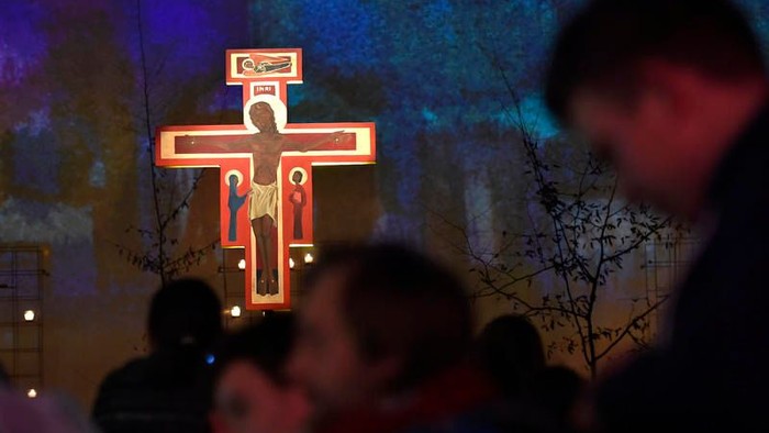 Eine Gruppe von Menschen betet vor einem beleuchteten Kreuz mit Jesusdarstellung.