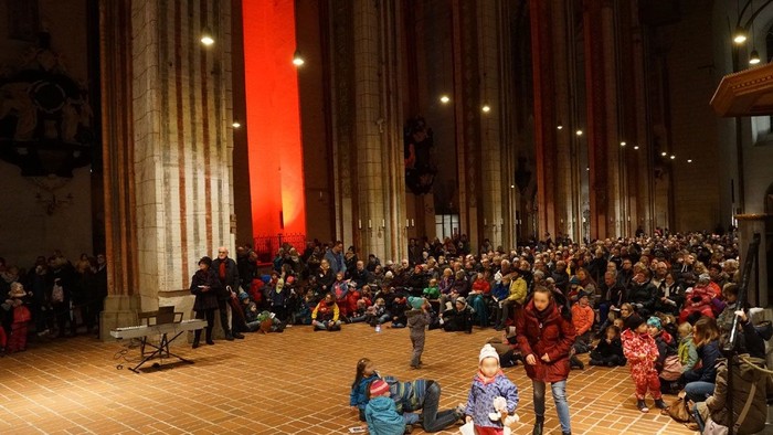 Große Menschenmenge in einem großen Raum mit hohen Säulen und roter Beleuchtung