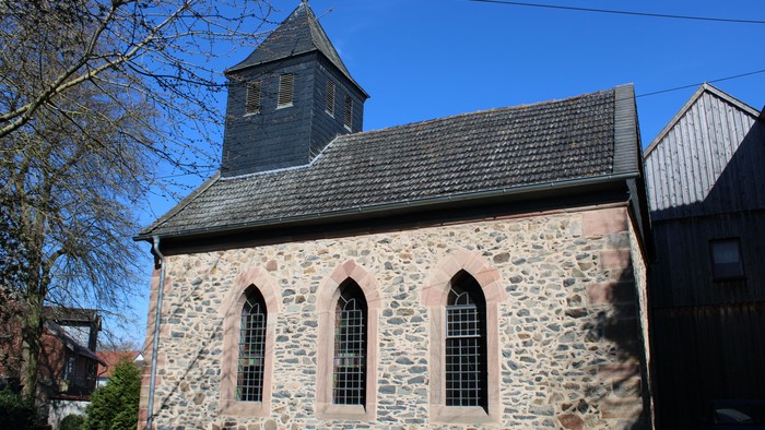 Steinkirche mit hohem, spitzem Turm und Rundbogenfenstern.