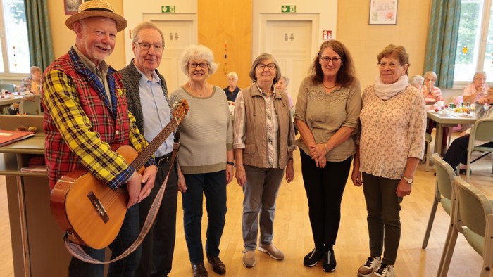 Eine Gruppe von sechs älteren Menschen posiert in einem Raum, einer spielt Gitarre
