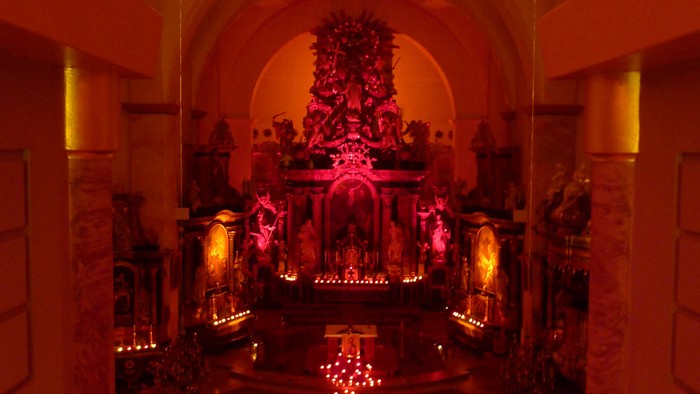 Lebhaft beleuchteter Kapelleninnenraum mit leuchtenden Kerzen und einem prunkvollen Altar, geschmückt mit Blumen.