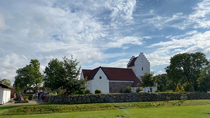 En hvid kirke med rødt tag og tårn i en grøn og åben mark