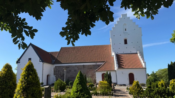 En fredelig kirke med et højt klokketårn og en velplejet have under en klar blå himmel.