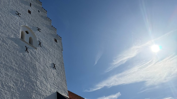 En hvid kirkebygning med rødt tag på en solskins dag med hvide skyer på himlen.