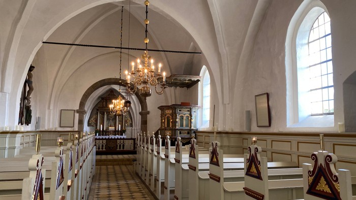 Indre del af kirke med hvidt indretning og hængende lygter