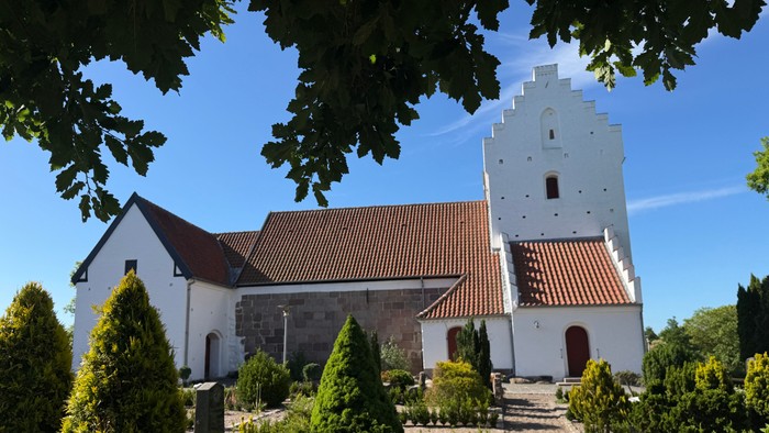 En fredelig kirke med et højt klokketårn og en velplejet have under en klar blå himmel.