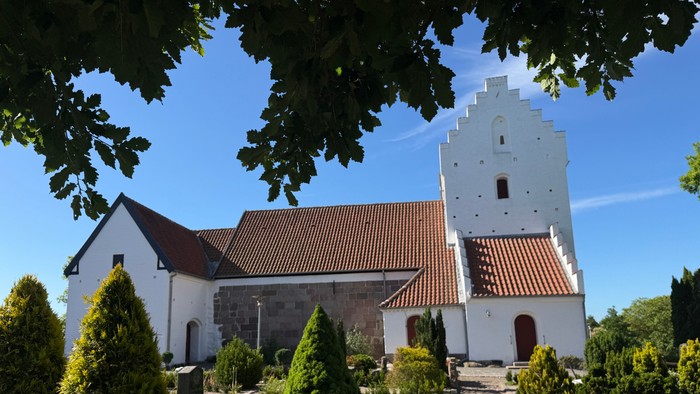 En fredelig kirke med et højt klokketårn og en velplejet have under en klar blå himmel.