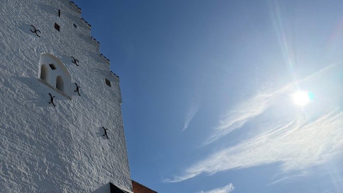 En hvid kirkebygning med rødt tag på en solskins dag med hvide skyer på himlen.