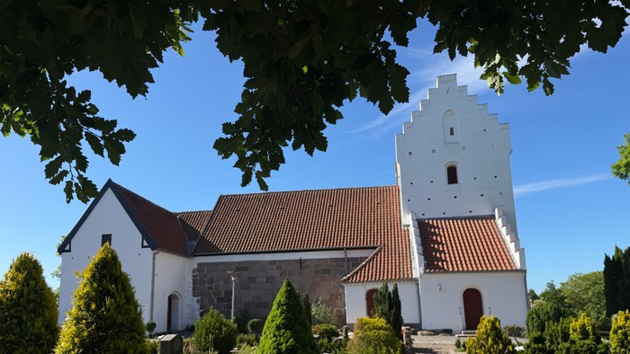 En fredelig kirke med et højt klokketårn og en velplejet have under en klar blå himmel.