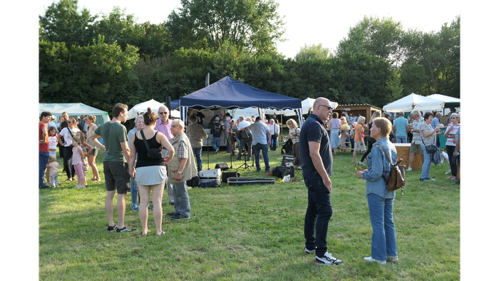 Freiluftmarkt mit Menschen, die unter Zelten in einer grünen Parklandschaft an Ständen stöbern.