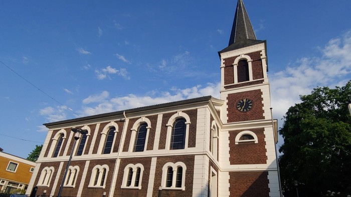 Das Bild zeigt eine Kirche mit hohem Turm und Zifferblatt unter blauem Himmel.