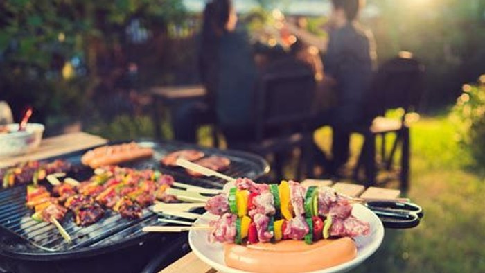 Farverige kebab spyd grilles udendørs, mens folk nyder en solrig havefest.