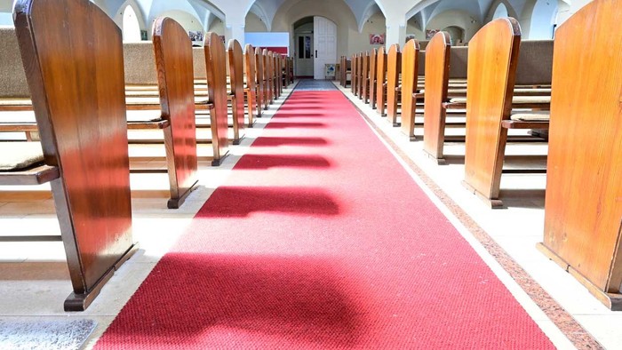 Leere Holzbänke in Kirche mit rotem Teppich.
