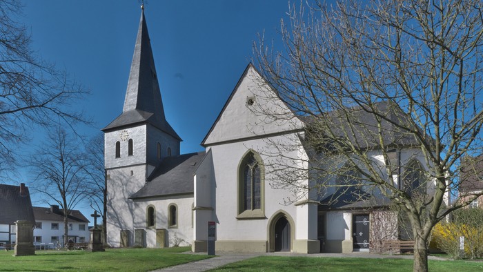 Eine friedvolle weiße Kirche mit hohem Kirchturm erhebt sich inmitten einer ruhigen, grünen Dorflandschaft.