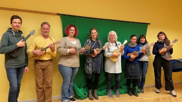 Gruppe von Menschen, die Ukulelen halten und vor grünem Hintergrund posieren.