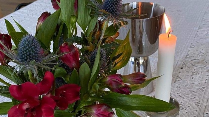 Blomster i en vase og stearinlys på en hvid blondedug.