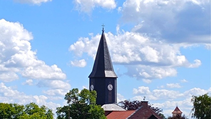 Kirchturm mit Uhrwerk vor blauem Himmel und weißen Wolken