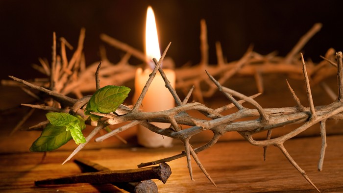 Im Zentrum des Bildes brennt eine Kerze, umgeben von Dornen und einem grünen Blatt, mit zwei Nägeln davor.