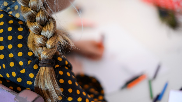 Et barn med en frisure og polkadottrøje sidder ved et bord og tegner.