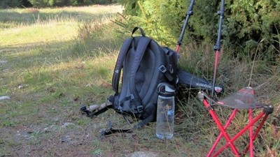 Vandretursudstyr inklusive rygsæk, vandrestave, vandflaske og sammenklappelig stol sat op udendørs på et græsareal.
