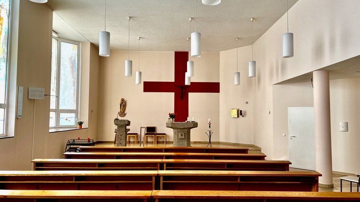 Die Kirche mit Holzbänken und einem großen roten Kreuz.